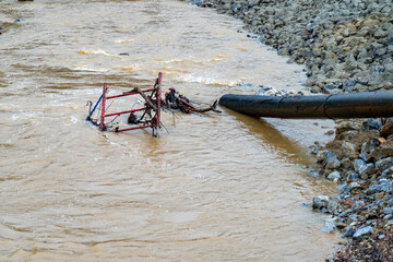 Construction equiment under fast moving water along a rocky embankment.