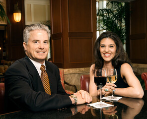 Prime adult Hispanic female and Caucasian prime adult male sitting at bar looking at viewer smiling.