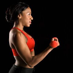 Profile of African American young adult woman lifting dumbbell.
