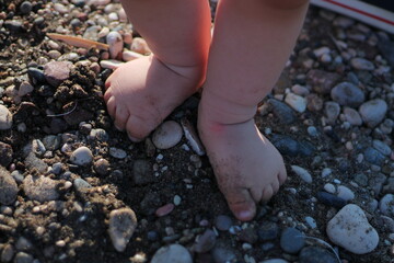 Baby son doing first steps on the beach. Bare feet staying on the sand. Summertime holidays concept. Top view