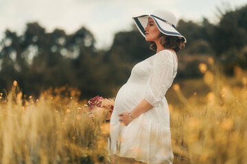 Embodying the spirit of Mother's Day, a pregnant woman in a white dress and hat carries a basket of...