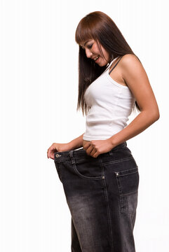 Attractive slim woman demonstrating weight loss by wearing an old pair of jeans and holding out to show how big the pants are