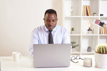 african american businessman sitting at the office table behind a laptop. Happy black employee not stressed, relaxing, watching funny video after successful work