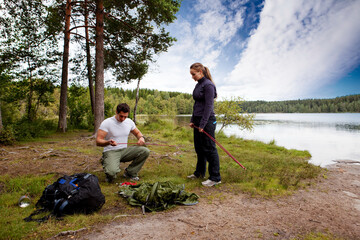 Camping lifestyle - a man and woman setting up a tent by a lake