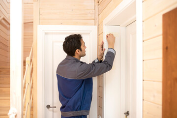 Fototapeta na wymiar Installation of a wooden door. Portrait of young handyman in blue uniform installing door. Professional repair service and maintenance concept