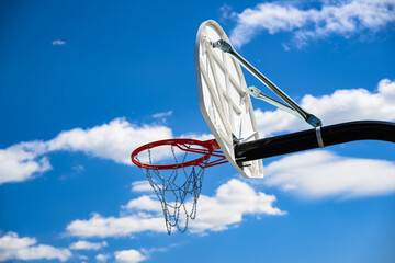 A new basketball backboard with a new hoop and metal netting has a beautiful blue sky with white...