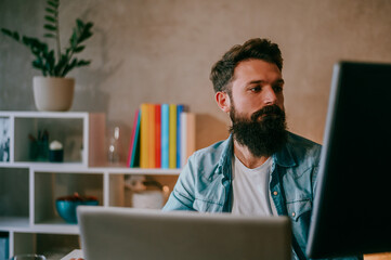 A preoccupied IT expert is sitting at his modern home office and working on software development surrounded by two monitors.