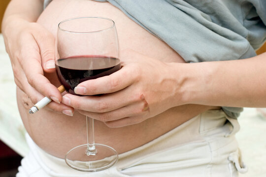 Young pregnant woman holding wine and cigarette