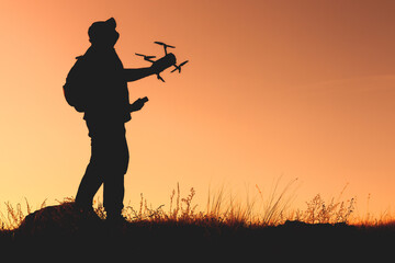 outside, the silhouette of a man with a quadcopter in his hands looks into the sky to launch a drone