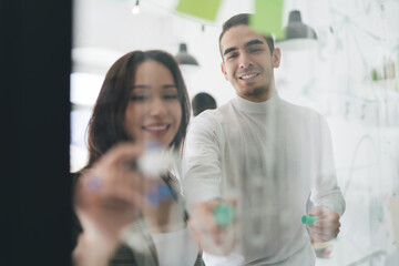 Obraz premium Cheerful young colleagues standing and working on project at glass wall in office