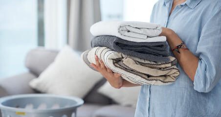 Hands, laundry and spring cleaning with a woman holding a pile of fresh towels in the living room...