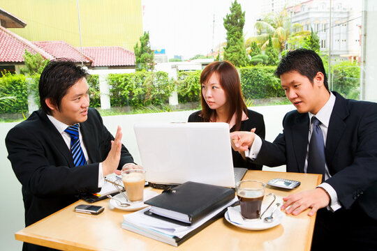 Situated in a café, a group of business people seriously discuss about something, with clean green environment of suburb area in the city as background.