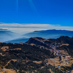 View of the beautiful Kuri village of Kalinchowk, Nepal from the top of a mountain with the clouds and mountains in the distant.