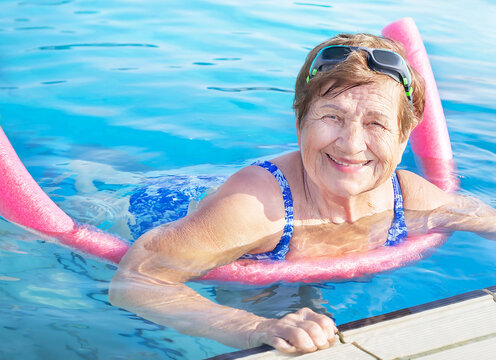 Active senior (elderly) woman (over age of 50) doing aqua fitness with swim noodles in swimming pool. Healthy lifestyle.