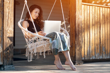 young female rest on macrame swing chair with laptop at country house terrace © goami