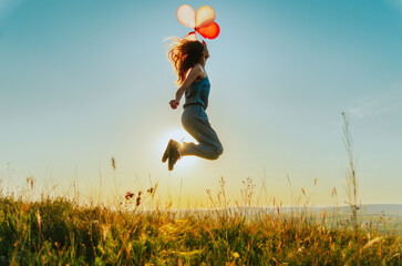 Silhouette of a young woman jumping with balloons on a hill backlit by sunset golden light