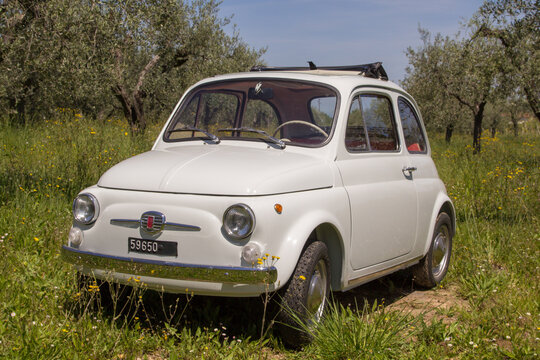Image of an old vintage Italian Fiat 500 car parked in the middle of a green field
