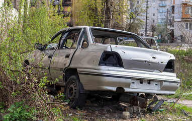 A broken Ukrainian civilian car, shot by artillery, stands in the courtyard of a destroyed house....