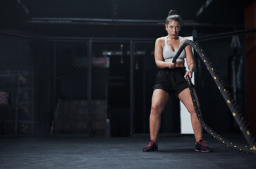 Obraz na płótnie Canvas Sports, battle ropes and woman at the gym doing strength, cardio and challenge exercise with space. Fitness, energy and strong female athlete doing health workout or training with equipment for power