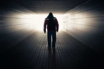 A man walks towards the light through a long blurry tunnel