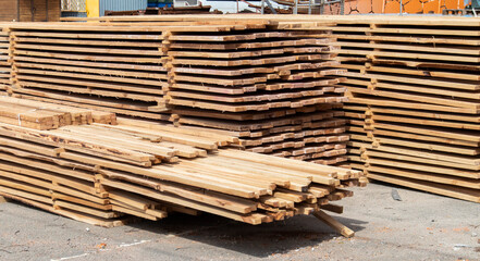 Pile of stacked wooden planks at a construction site. Wooden boards, lumber. Industrial edged timber. Wooden rafters for the repair or construction of a private house. Roofing and joinery lumber.