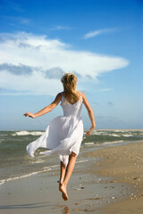 Fototapeta na wymiar Caucasian pre-teen girl running down the beach in flowing white dress.