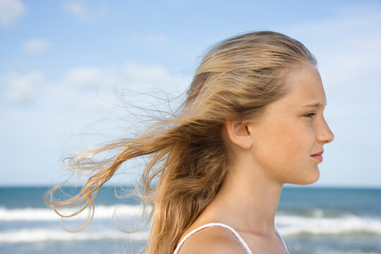 Caucasian pre-teen girl on beach with hair blowing in wind.