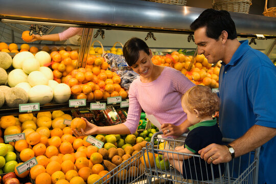 Caucasian mid-adult parents grocery shopping for fruit with male toddler.