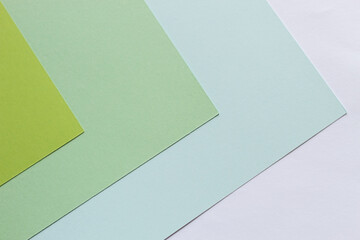 Sheets of paper of green shades lie on the table with corners in one direction.