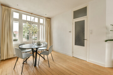 a dining table and chairs in a room with large windows looking out onto the street below, there is a pot of flowers on