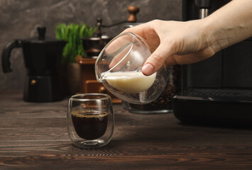 

Black coffee in a glass and cream. Pour cream or milk into espresso. Coffee drink on black table background.Barista. Coffee house concept. Place for text.