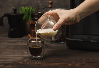 Fototapeta na wymiarBlack coffee in a glass and cream. Pour cream or milk into espresso. Coffee drink on black table background.Barista. Coffee house concept. Place for text.