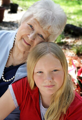 A pretty blond girl and her grandmother in the garden.  The little girl looks serious.  Vertical view.