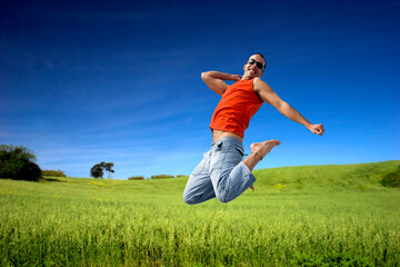 Man jumping on a green meadow with a beautiful cloudy sky