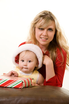 Adorable caucasian blond baby girl toddler sitting with mom a wearing Santa cap