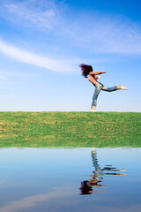 Woman jumping on green field, with water reflection.