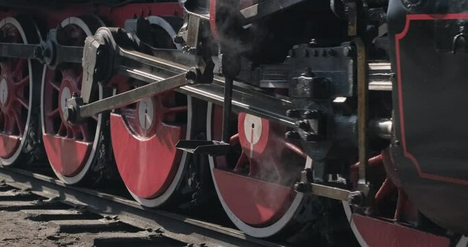 Old steam locomotive moving on rails, low angle close up shot of rotating wheels and machinery, static handheld camera, natural lighting.