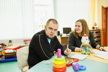 an autistic adult is undergoing rehabilitation with an assistant in the classroom - obrazy, fototapety, plakaty