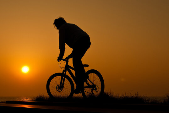 silhouet of a young adult riding a bike at sunset