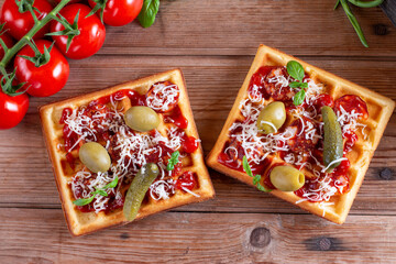 Pizza waffle toast with tomatoes, cucumber, olives, sausages, cheese and herbs on a table. Top view.