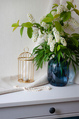 Interior decor. Flowers in a blue glass vase, a golden candlestick and pearl beads. Selective focus