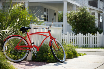 Red beach cruiser bicycle propped against fence in front of house.