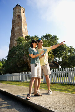 Mid-adult Caucasian couple sightseeing with lighthouse in background at Bald Head Island, North Carolina.
