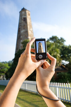 Close up of Caucasian woman's hands holding digital camera and photographing lighthouse at Bald Head Island, North Carolina.