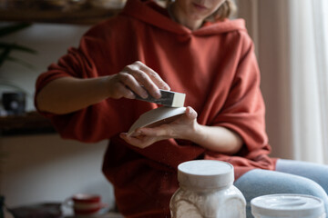 Closeup hands woman ceramist with saucer and hard sponge for cleaning bumps from dishes after...