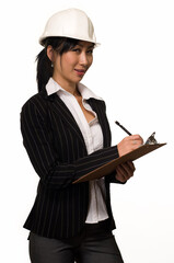 Asian woman in business suit wearing a white safety hard hat holding and writing on a chart