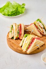 Club sandwiches with chicken, boiled egg, tomato and bacon on a wooden board on a light concrete background. American cuisine.