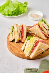 Club sandwiches with chicken, boiled egg, tomato and bacon on a wooden board on a light concrete...