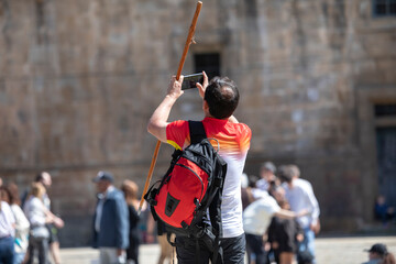 Pilgrims on the Camino de Santiago arrive at the Plaza del Obradoiro because they have finished their pilgrimage. A pilgrim takes photos of the cathedral of Santiago de Compostela with his mobile phon