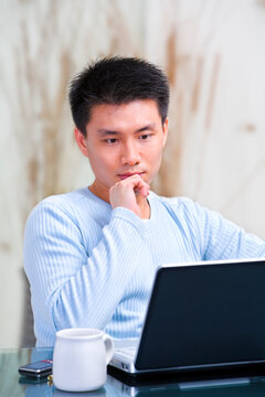 portrait of young Chinese man thinking in front of his laptop at home.